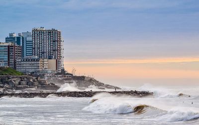 Sea by buildings against sky during sunset