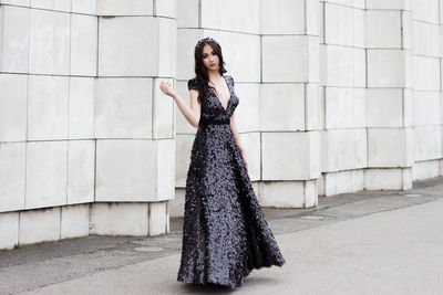 Portrait of beautiful woman wearing evening gown while standing against wall