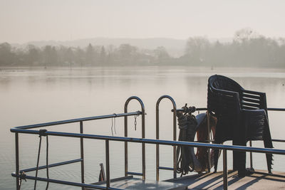 Man sitting on railing by lake against sky