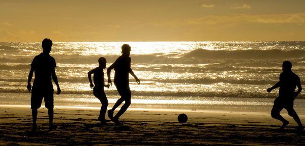 Silhouette men playing soccer at beach against sky during sunset