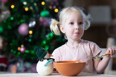 Cute blond toddler girl with blue eyes having her meal in new year entourage. girl is left-handed.