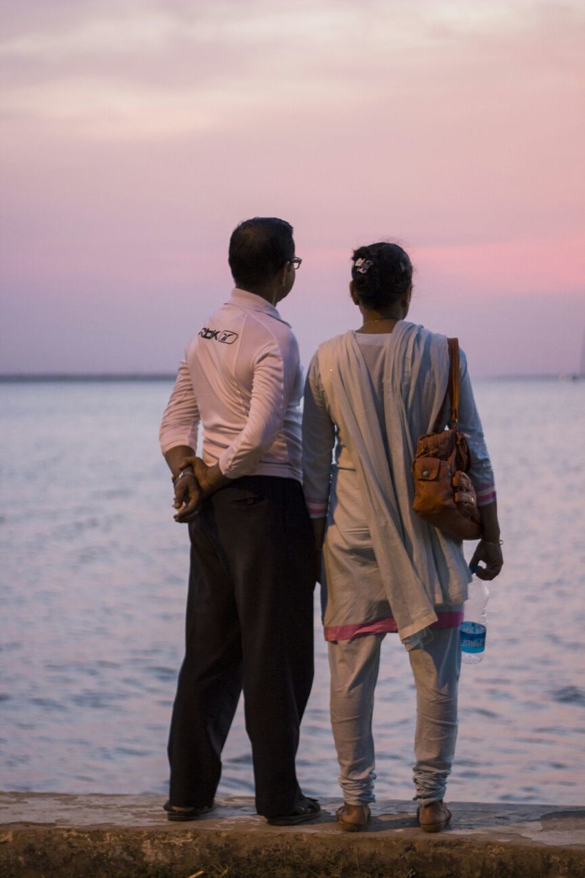 rear view, togetherness, lifestyles, sea, leisure activity, bonding, men, water, love, sky, standing, person, sunset, horizon over water, beach, casual clothing, friendship, full length