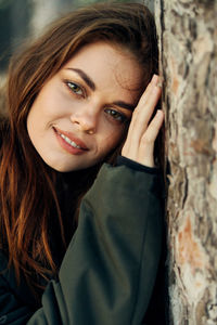 Portrait of smiling young woman by tree trunk