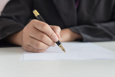 Midsection of man writing over paper while sitting on table