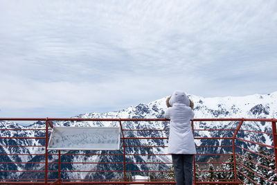 Rear view of person standing by railing against sky during winter