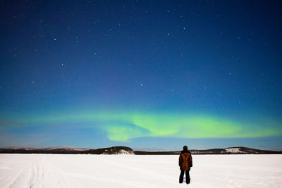 Rear view of man standing on snow covered land against sky at night
