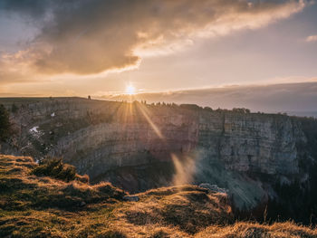 View of sun shining through clouds over land