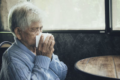 Old person coughing covering mouth with a tissue on a house interior. she has flu, allergy symptoms.