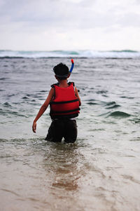 Rear view of boy playing at beach against sky