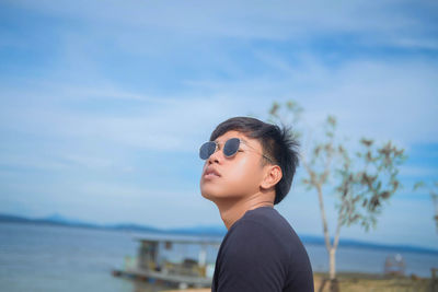 Young man wearing sunglasses while looking away against sky