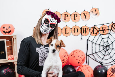 Portrait of woman wearing mask holding dog at home