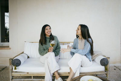 Happy female friends talking while sitting with drinks in backyard