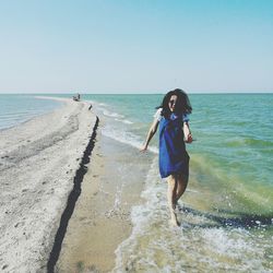 Full length of woman splashing water at beach on sunny day