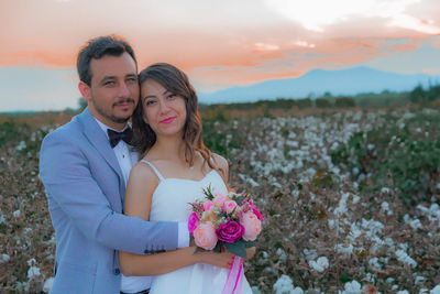 Portrait of smiling bride and groom with bouquet romancing on field