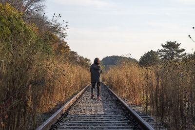 Rear view of woman standing on railroad track