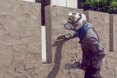 Side view of male plasterer applying cement on wall