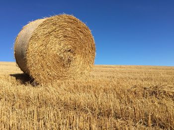 Hay bales on field against clear blue sky