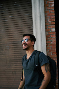 Young man wearing sunglasses standing against brick wall