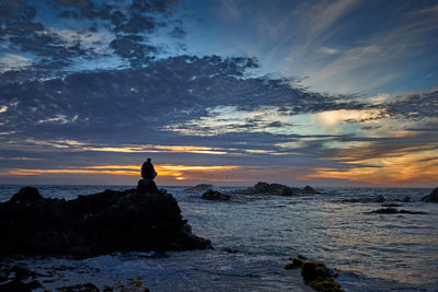 Silhouette rocks on sea against sky during sunset