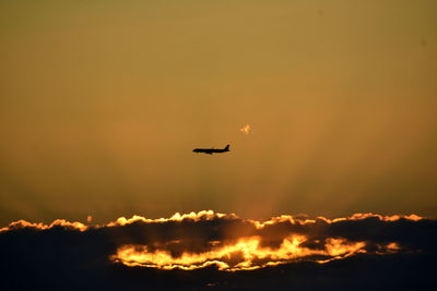 Low angle view of silhouette airplane flying against orange sky