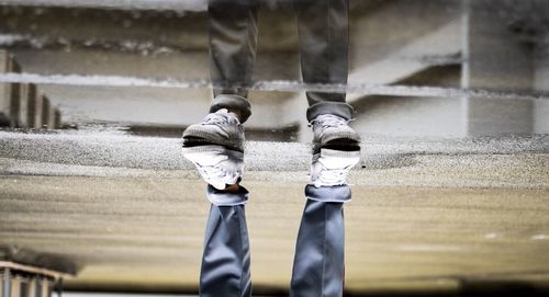 Low section of men reflecting in puddle while standing on footpath