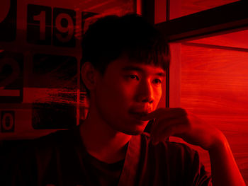 Thoughtful young man looking away in red illuminated home