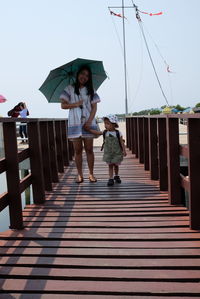 Full length of mother and daughter standing on pier against sky