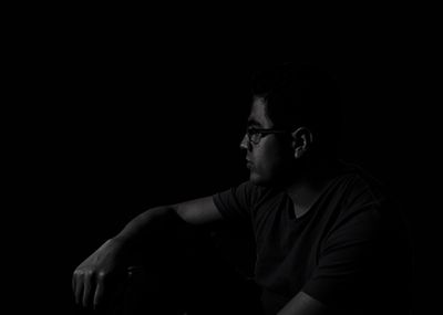 Thoughtful man looking away while sitting against black background