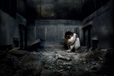 Frightened teenage girl sits alone in a ruined house