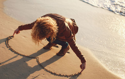 High angle view of woman making heart shape on sand at beach