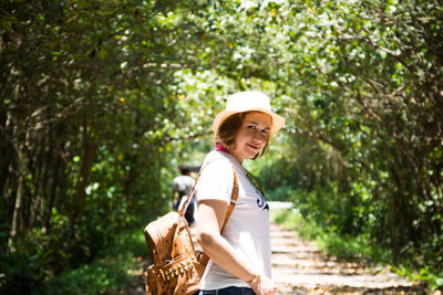 Portrait of smiling woman standing against trees during sunny day