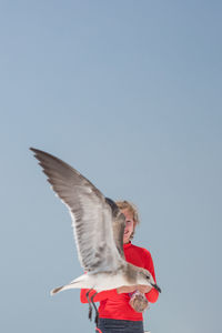 Girl standing by seagull flying 