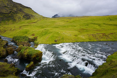 Scenic view of stream flowing by land against sky