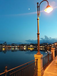 Illuminated street light by buildings against sky at night