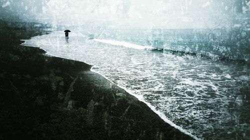 Man with umbrella walking on shore at beach