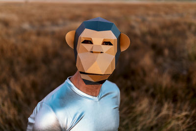 Anonymous person in geometric monkey mask looking at camera in yellow field on blurred background