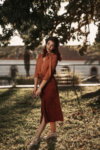 Portrait of young woman standing on grass against trees