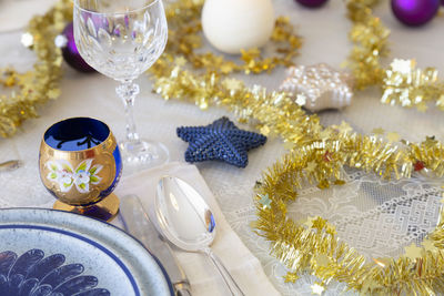 A decorated dining table with burning candles, cutlery, glasses, colorful christmas balls and tinsel