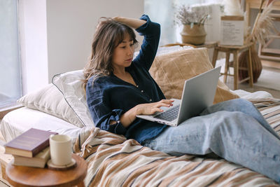 Woman using laptop on bed at home