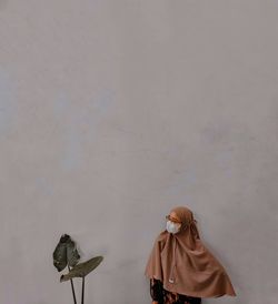 Woman standing by plant against wall