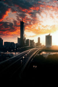 Road by buildings in city against sky during sunset