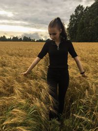 Beautiful woman touching crops while standing on field against sky during sunset