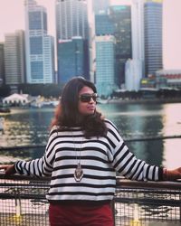 Woman wearing sunglasses while looking away against buildings in city