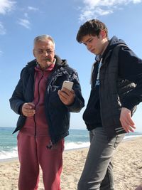 Man showing mobile phone to grandson while standing at beach