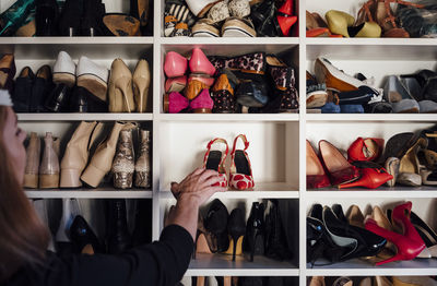 Cropped unrecognizable woman hands taking beige high heels shoes from shelf of modern white closet