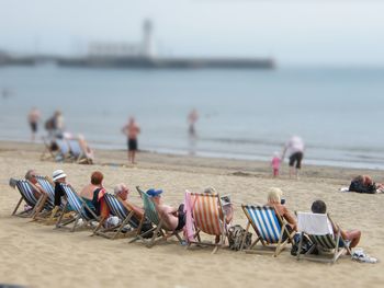 Tilt-shift image of people relaxing on deck chairs at beach