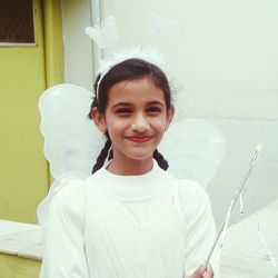 Portrait of smiling girl wearing angel costume against wall
