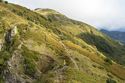 Young woman in yellow hoodie  with backpack hiking in picturesque mountain valley healthy lifestyle 