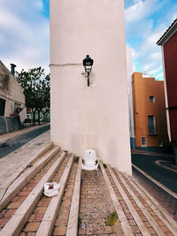 Empty plastic chair on stairs between two streets and in front of a white wall and a lantern