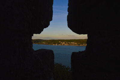 Silhouette rock formation by sea against sky